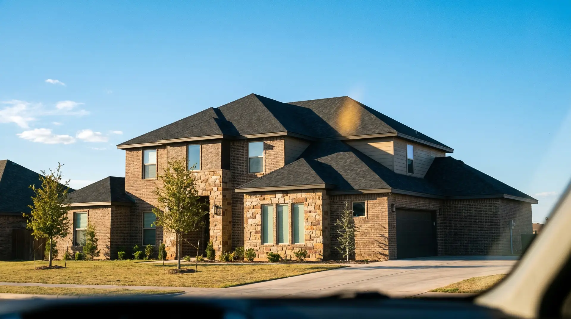 A roofer installing the best roof shingles for Lubbock, impact-resistant charcoal shingles, on a modern brick home with a nail gun